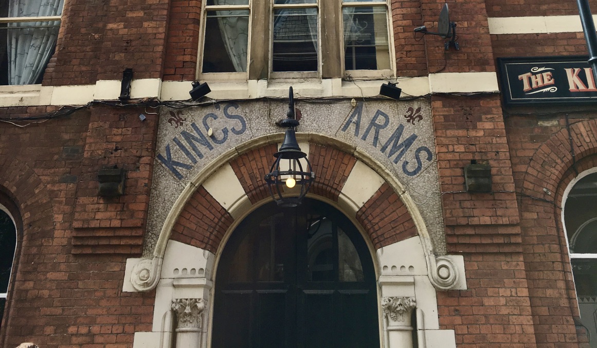 The entrance to the Kings Arms pub, a red brick building with its name set in the stone arch above the door.