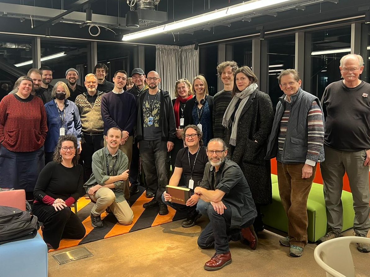 A group of around 20 people are bunched together or crouching to pose for a group photo. Everyone is grinning happily. 