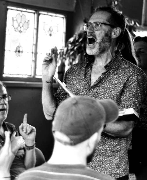 Leading a song in the Frog House - Manchester Sacred Harp at the Frivolous Fields folk festival in Platt Fields Market Garden, June 2025