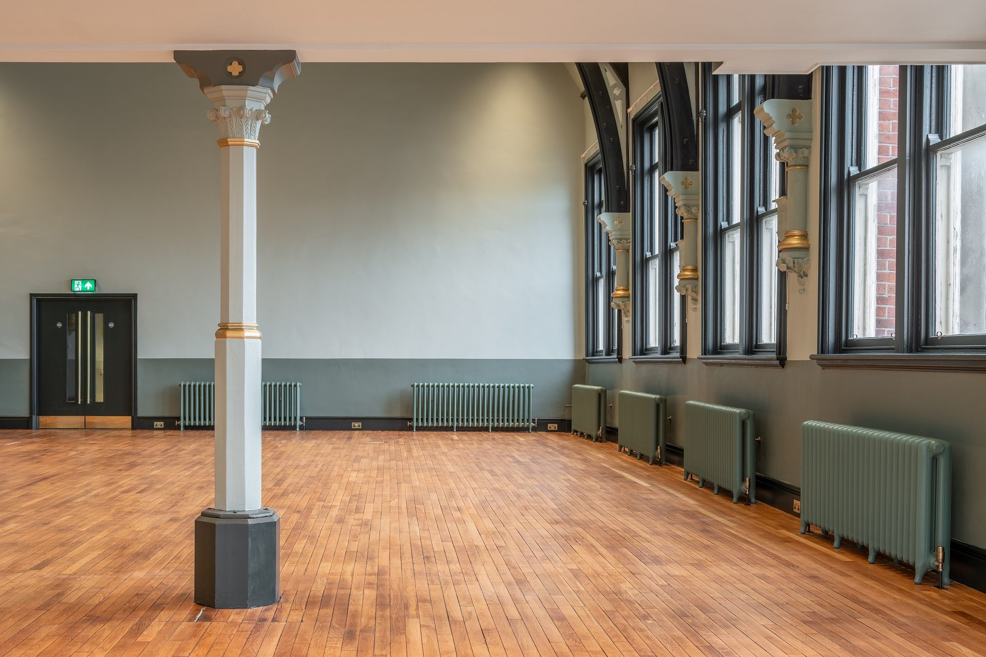 In a large room a narrow pillar holds up the mezzanine floor, beyond which we see the beginning of the arches up to the high ceiling, a row of windows and a smooth, gleaming oak floor. All the Victorian details have been picked out in tasteful green and gold. The room is bright, empty and spacious.