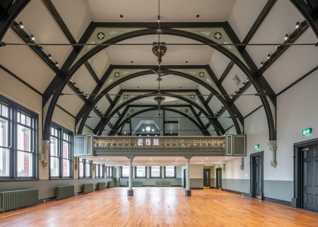 A magnificent large room with wooden arches in the high ceiling, rows of windows along two sides and a gleaming oak floor. All the Victorian details have been picked out in tasteful green and gold. The room stretches before us, bright and breathtaking in its scale. 
