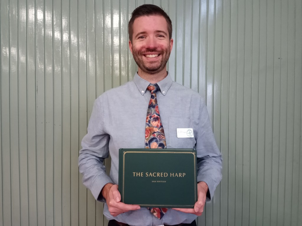 Matthew Parkinson smiling as he holds the 2025 edition. He's wearing a fancy red and green tie