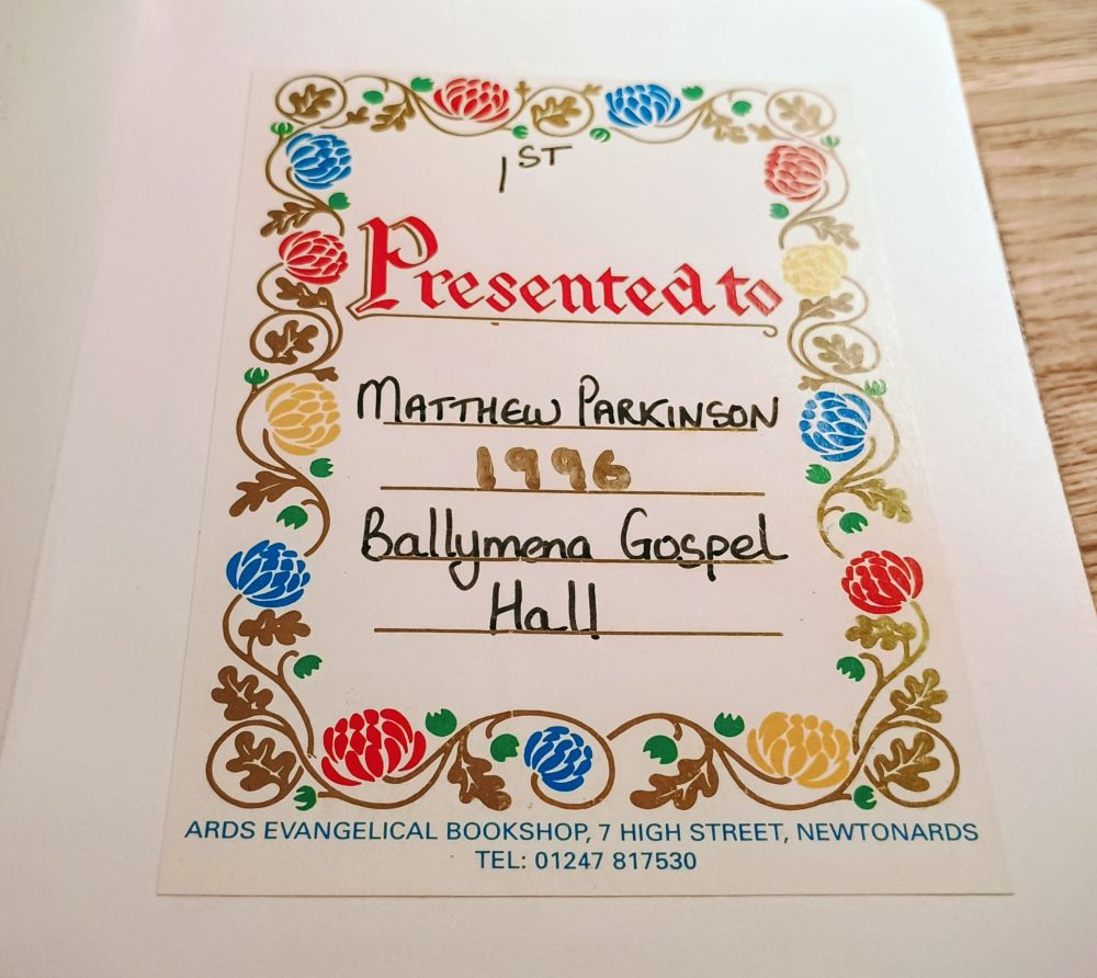 The inside page of a hymn book, with a very colourful floral border, and the words "Presented to Matthew Parkinson, 1996, Ballymena Gospel Hall"