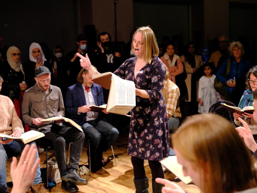Hannah leading the first singing at the Whitworth, at the launch of the Suzanne Lacy exhibition. Manchester regulars Mika, John, Jo and Tom are in the square; members of the Asian community are visible beyond them.