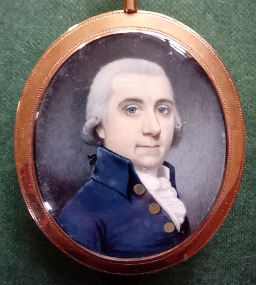 A painted miniature portrait in an oval frame, showing a man in (probably) late eighteenth-century dress: white frills visible under a blue jacket with brass buttons. He wears a grey wig and has pale blue eyes.