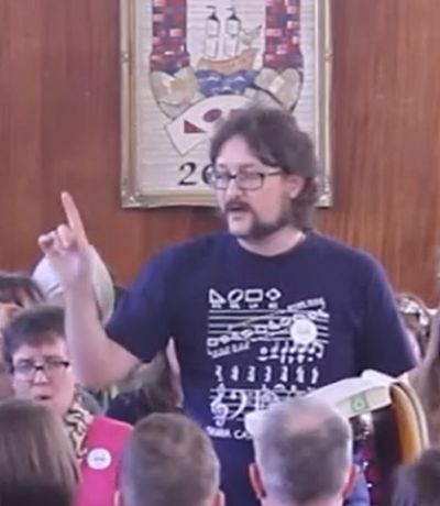 Jan leading 49b Mear at the Ireland Convention in Cork, March 2017. He is wearing a black and white Tshirt showing shapenotes and other musical notations, and is sporting magnificent Mutton Chops facial hair.
