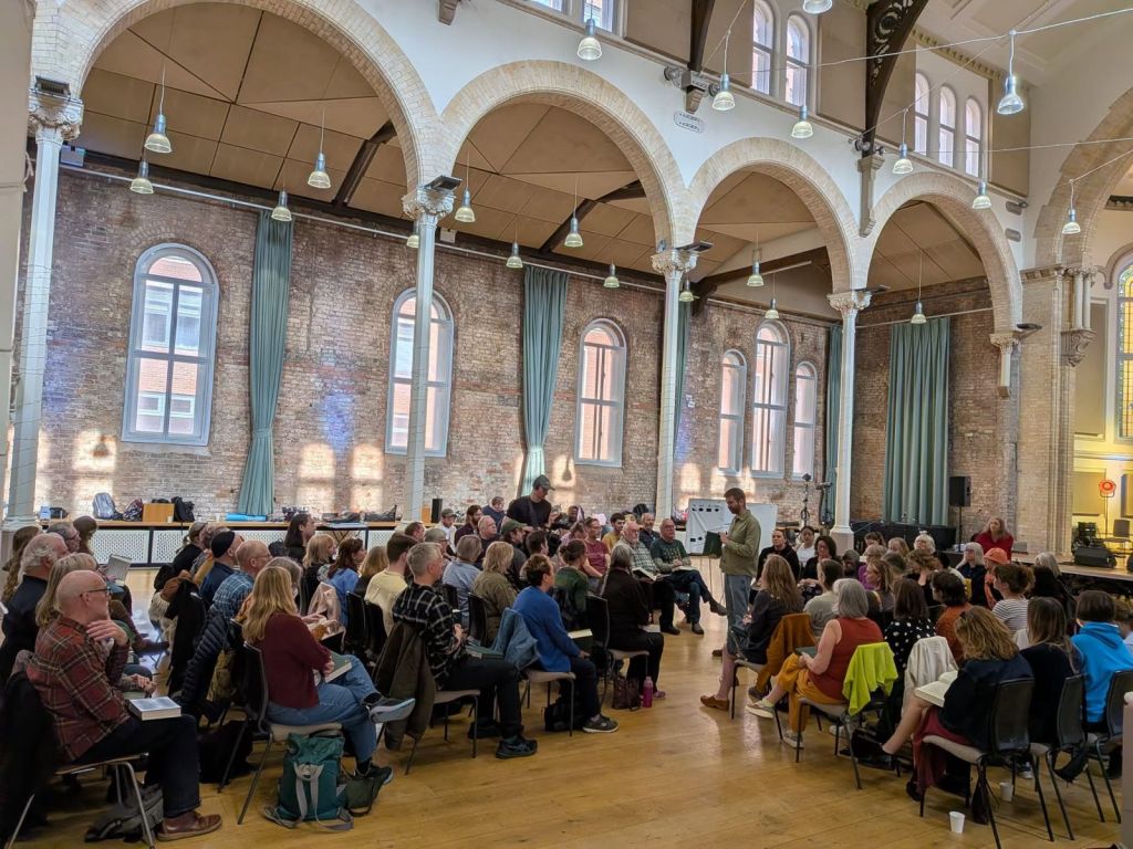 A large number of singers attending a singing school during the Manchester Folk Festival, with the arches of the former church of St Peter's in the background